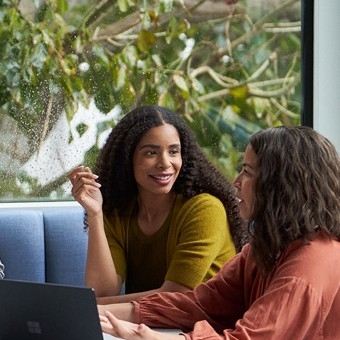 A woman smiles while listening to another woman explain an idea