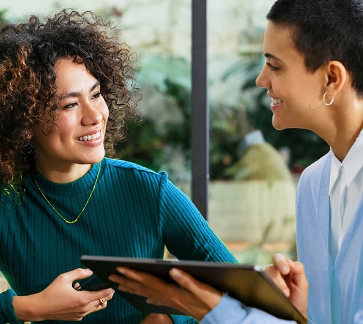 Two people smiling and talking while one is holding a tablet device