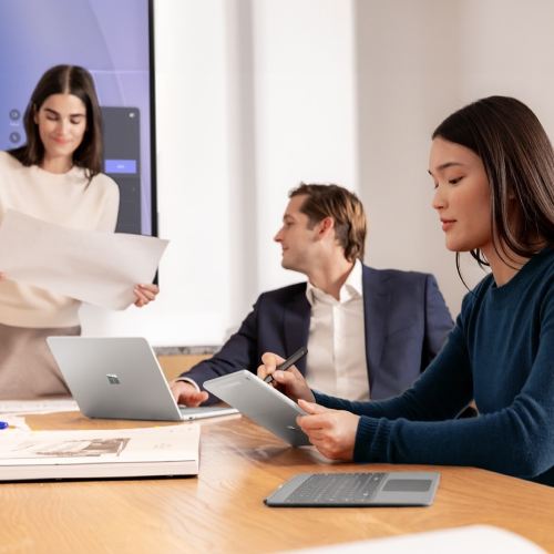 Three people in a meeting using computers and a large print-out to work on a project