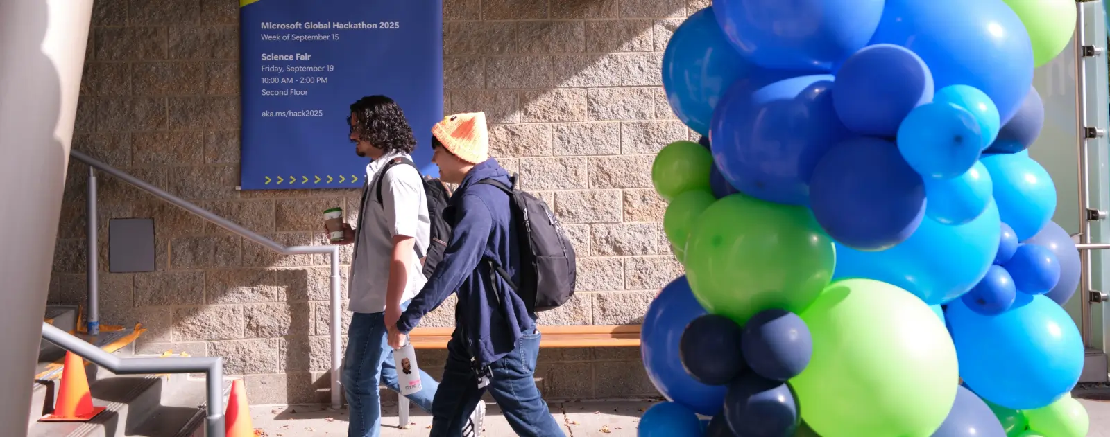 Two people walking by blue and green balloons.