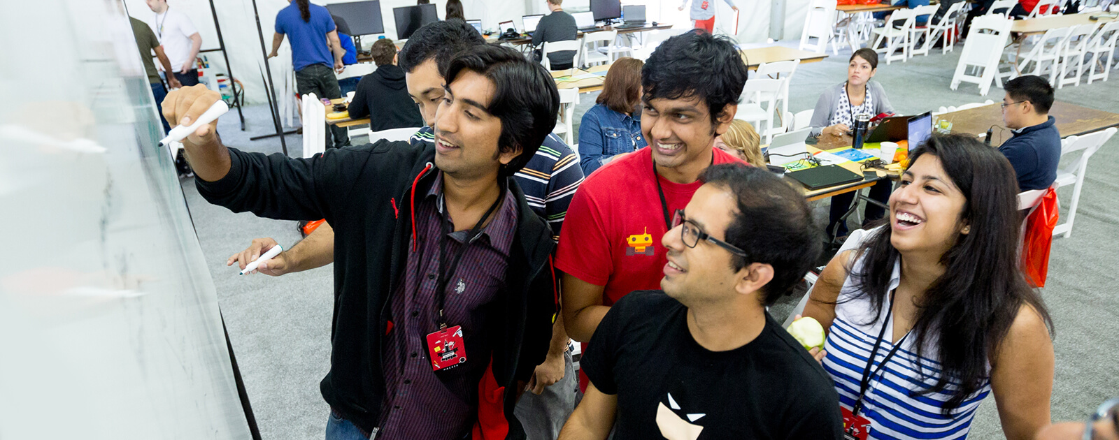 A group of people smile while working together at a whiteboard