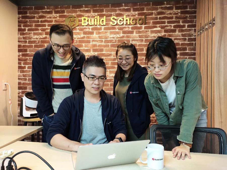 四個人身處 Build School 的場地，圍繞在筆電螢幕旁