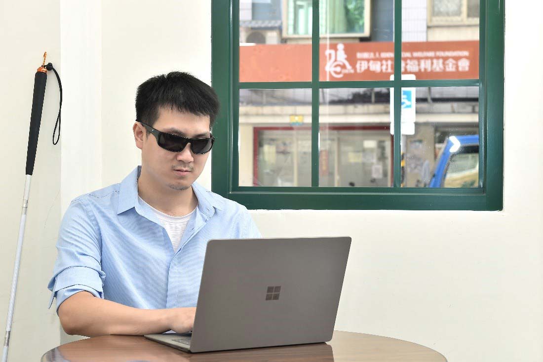 一張這位視障人士坐在椅子上，正學習使用著電腦的照片