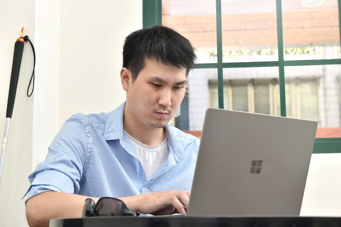 一張這位視障人士將墨鏡脫下，使用著電腦的照片