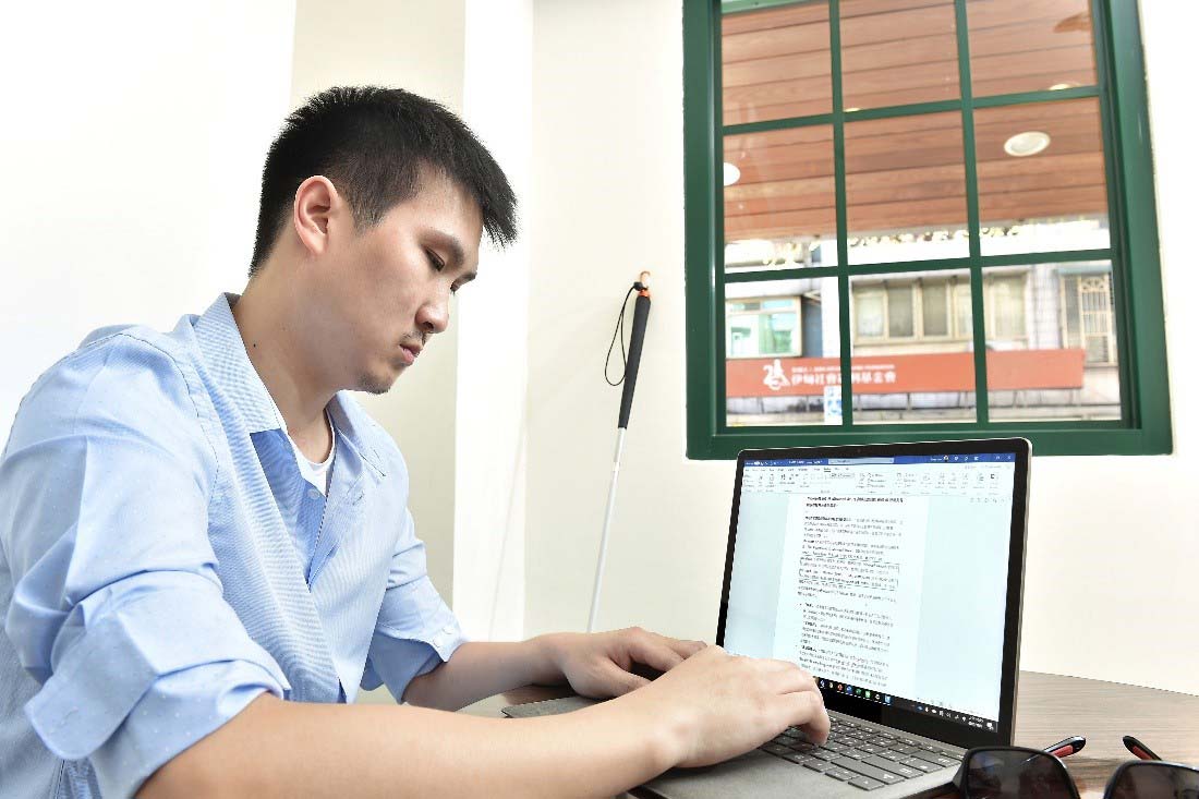 一張這位視障人士脫下墨鏡，正在打字的照片
